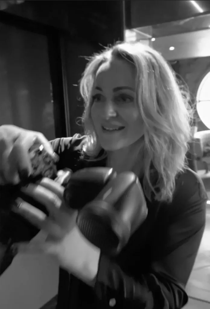 Zwart-witportret van een blonde vrouw die glimlachend met een camera in haar handen opzij kijkt