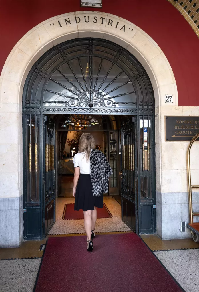 Vrouw loopt over een rode loper door een sierlijke boogdeur met het opschrift Industria